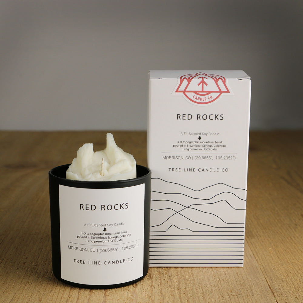 A white wax candle named Red Rocks is next to a white box with red and black lettering.
