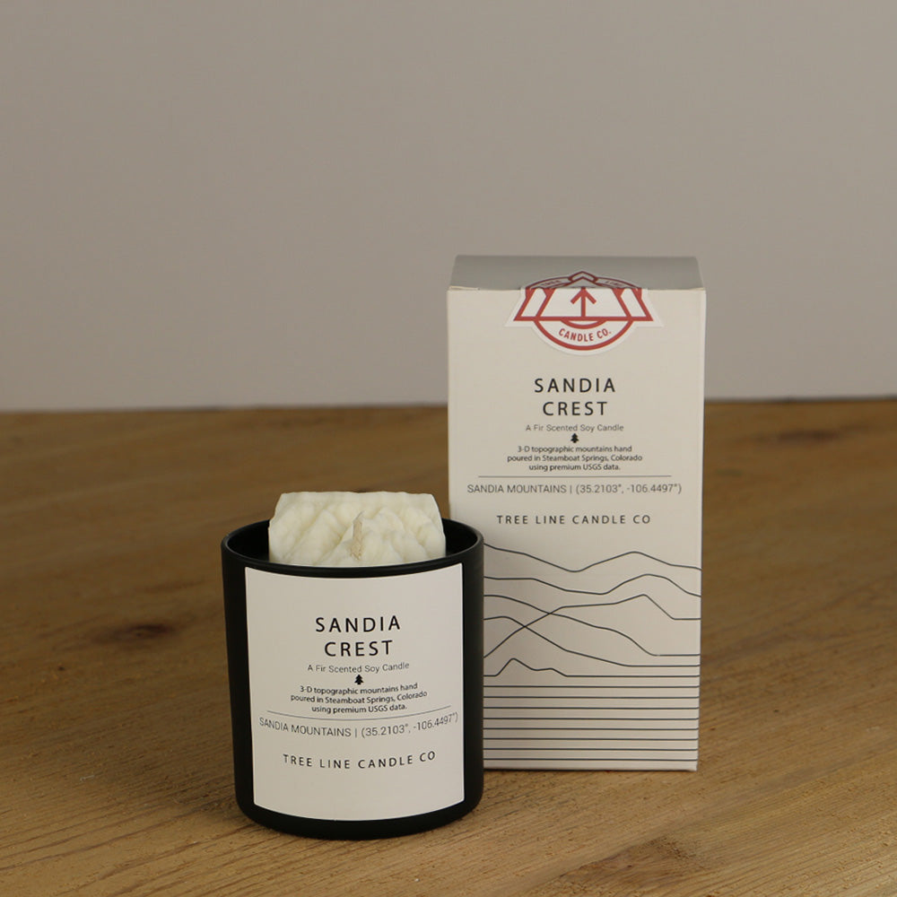 A white wax candle named Sandia Crest is next to a white box with red and black lettering.