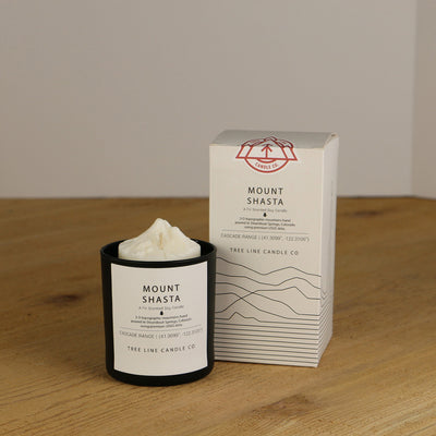 A white wax candle named Mount Shasta is next to a white box with red and black lettering.