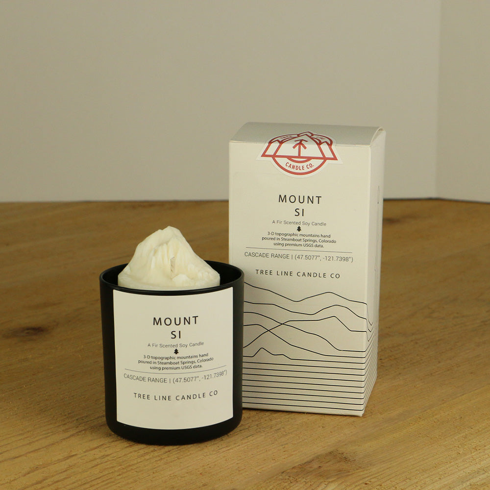 A white wax candle named Mount Si is next to a white box with red and black lettering.