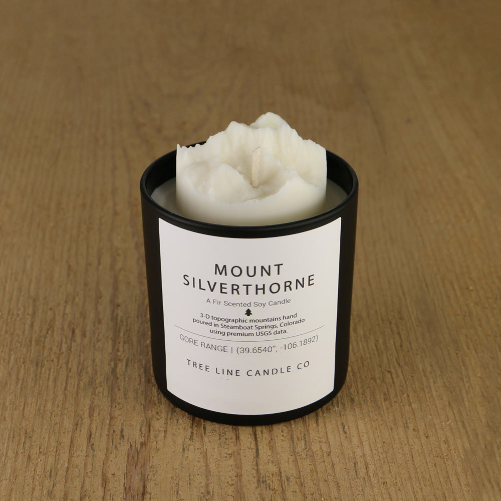 A white soy wax replica candle of Mount Silverthorne in a round, black glass.