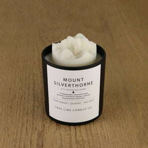 A white soy wax replica candle of Mount Silverthorne in a round, black glass.