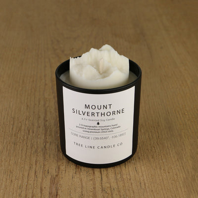 A white soy wax replica candle of Mount Silverthorne in a round, black glass.