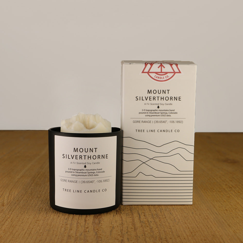 A white wax candle named  Mount Silverthorne is next to a white box with red and black lettering.