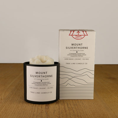 A white wax candle named  Mount Silverthorne is next to a white box with red and black lettering.