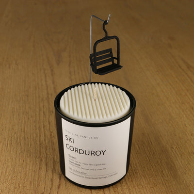 A white soy wax replica candle of SKI Corduroy in a round, black glass.