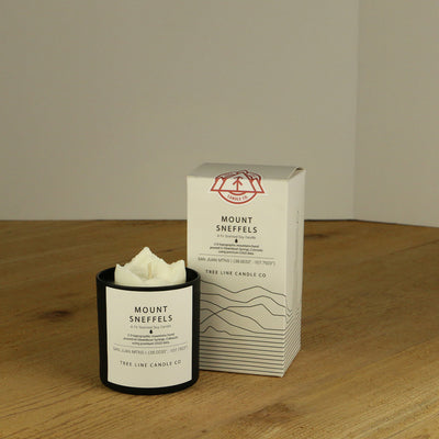 A white wax candle named Mount Sneffels is next to a white box with red and black lettering.