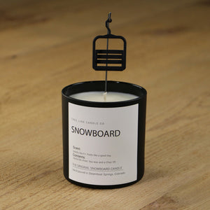 A white soy wax replica candle of  level snow with a gondola chair hanging over it in a round, black glass.