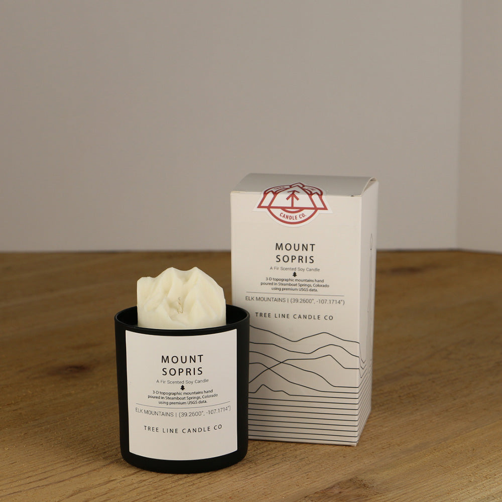 A white wax candle named Mount Sopris is next to a white box with red and black lettering.