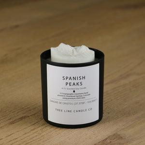 A white soy wax replica candle of Spanish Peaks in a round, black glass.