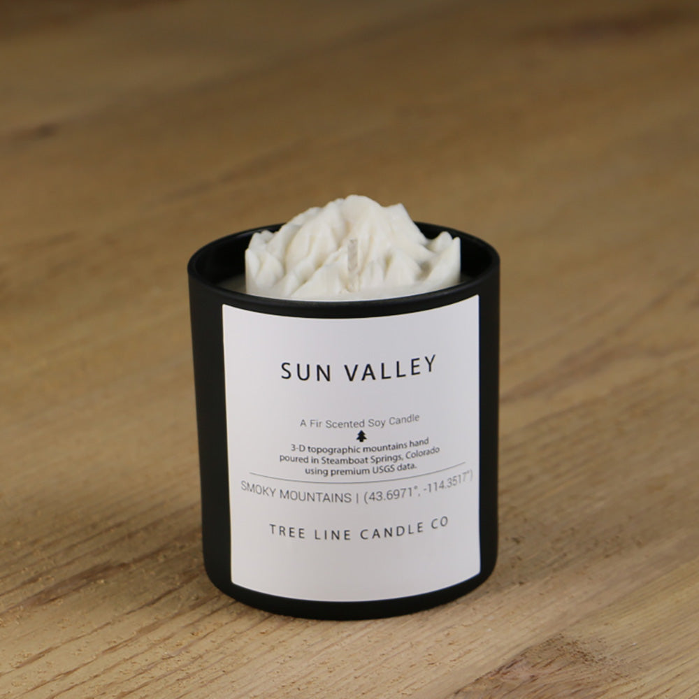 A white soy wax replica candle of Sun Valley mountain in a round, black glass.