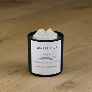 A white soy wax replica candle of Sunset Rock in a round, black glass.