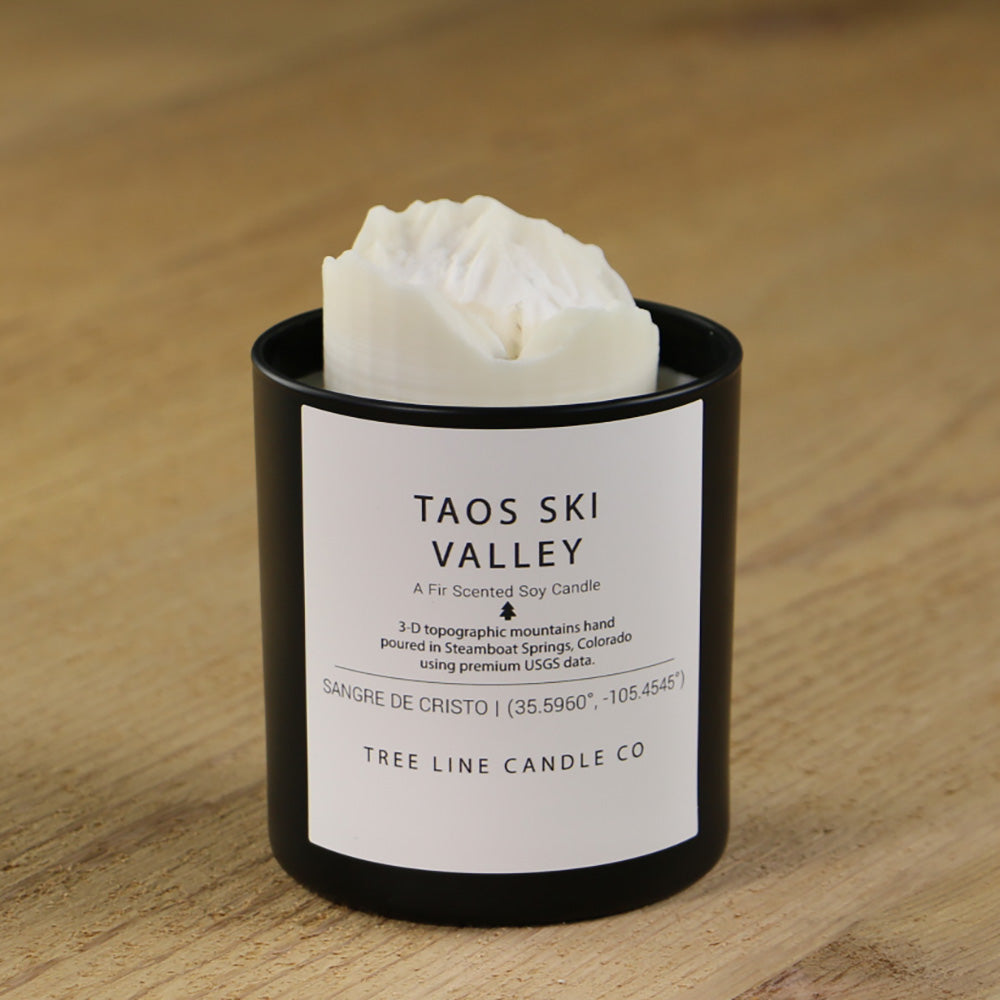 A white soy wax replica candle of Taos Ski Valley in a round, black glass.