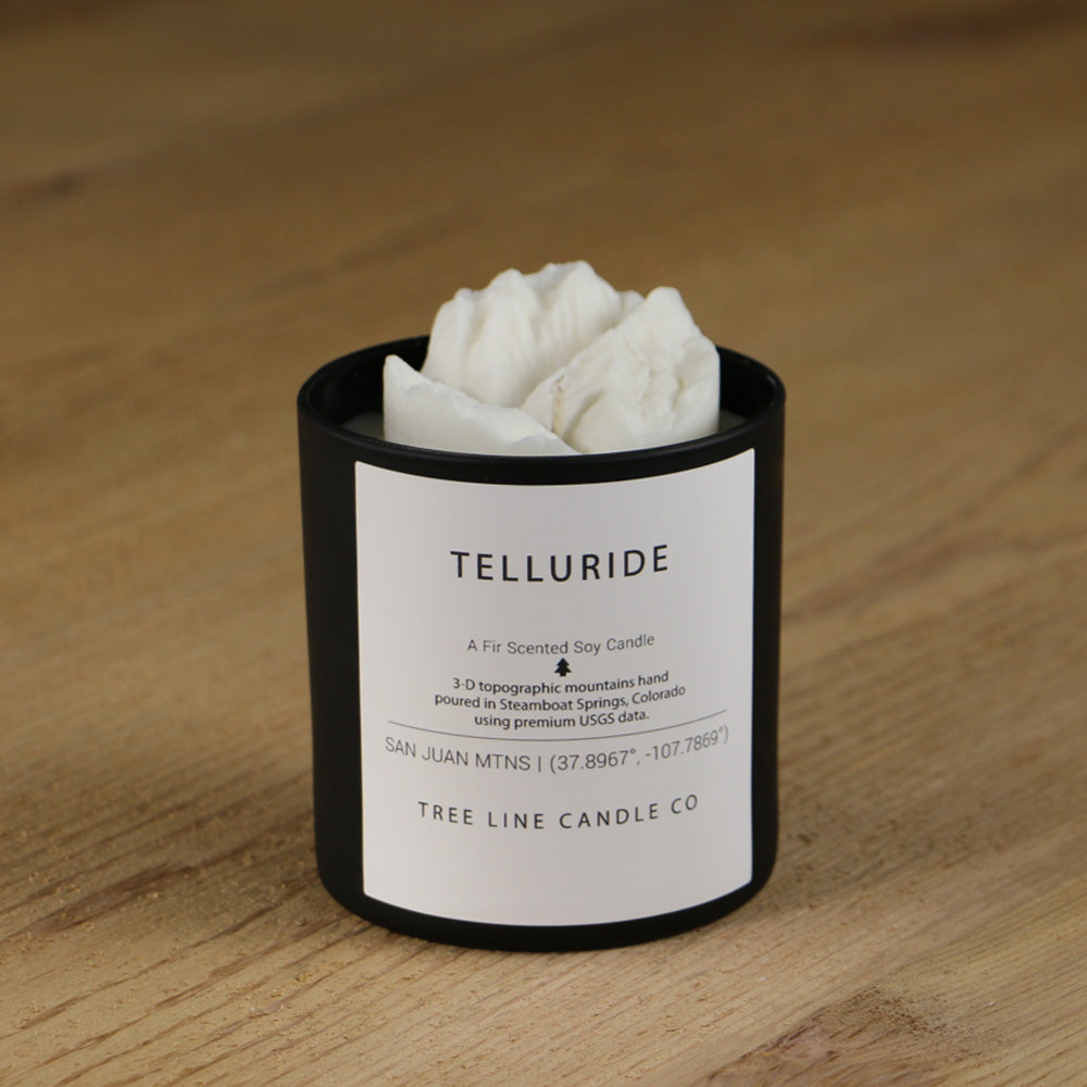 A white soy wax replica candle of Telluride summit in a round, black glass.