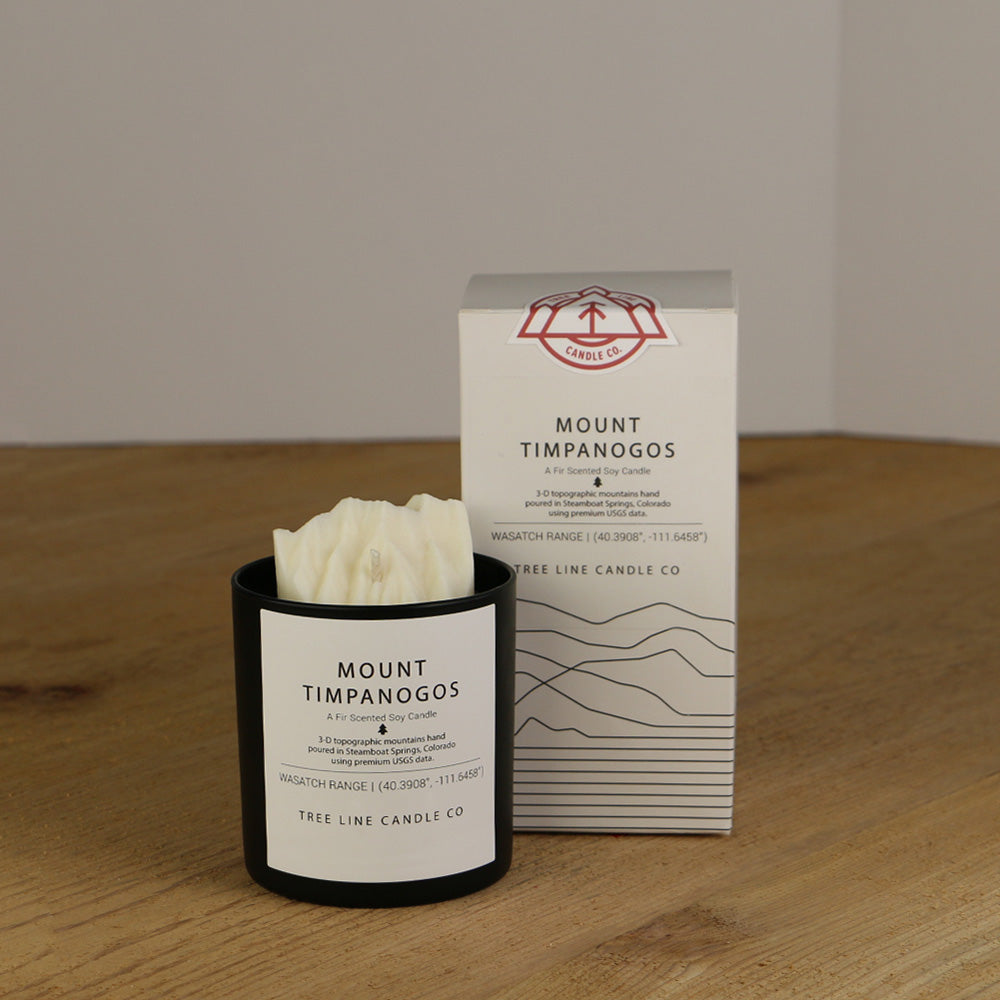 A white wax candle named Mount Timpanogos is next to a white box with red and black lettering.