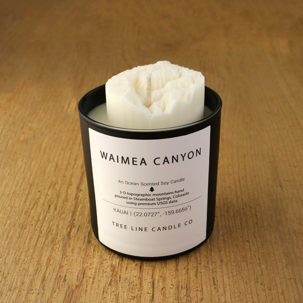 A white soy wax replica candle of Waimea Canyon in a round, black glass.