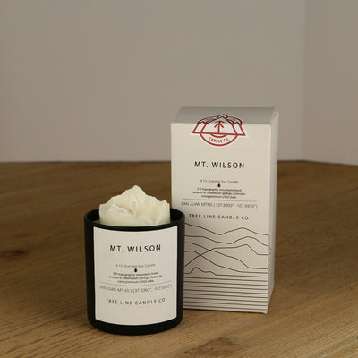 A white wax candle named Mount Wilson is next to a white box with red and black lettering.